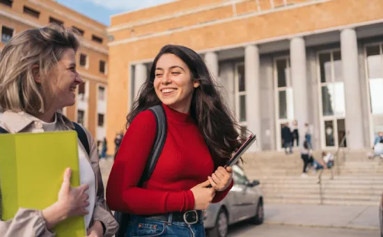 Oportunidades internacionales que enriquecen tu experiencia universitaria Dos estudiantes universitarias conversando frente a un edificio académico